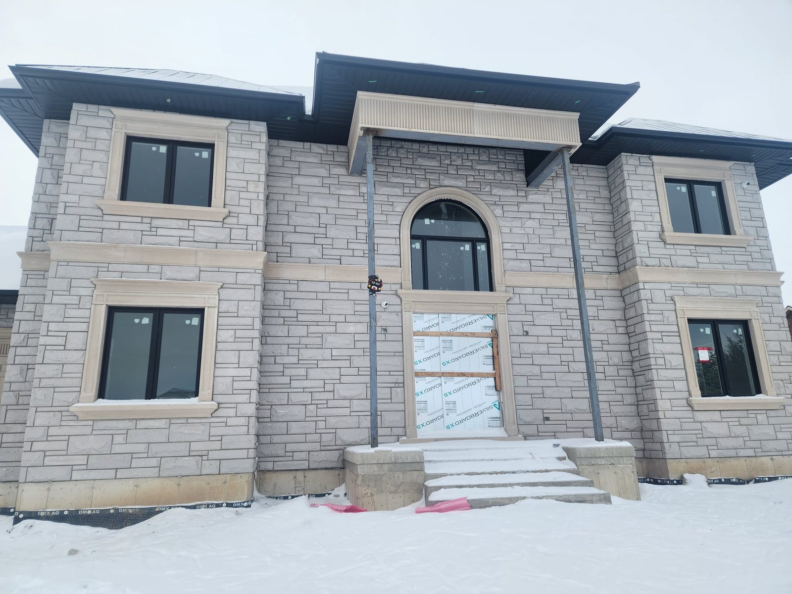 Finished stone home with arched entry viewed in winter conditions